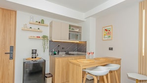 A compact kitchen with a refrigerator, microwave, wooden cabinets, and a small dining area with stools. - Edificio Bloom (Medellín)