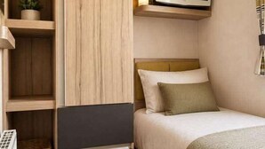 A compact room with a bed, a television, a wardrobe, and a small plant. - 3 Bedroom Caravan Alix (Rhyl)