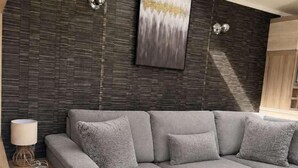 A modern living room with a grey sectional sofa, a wooden side table, a floor lamp, and a large abstract painting on the wall. - 3 Bedroom Caravan Alix (Rhyl)