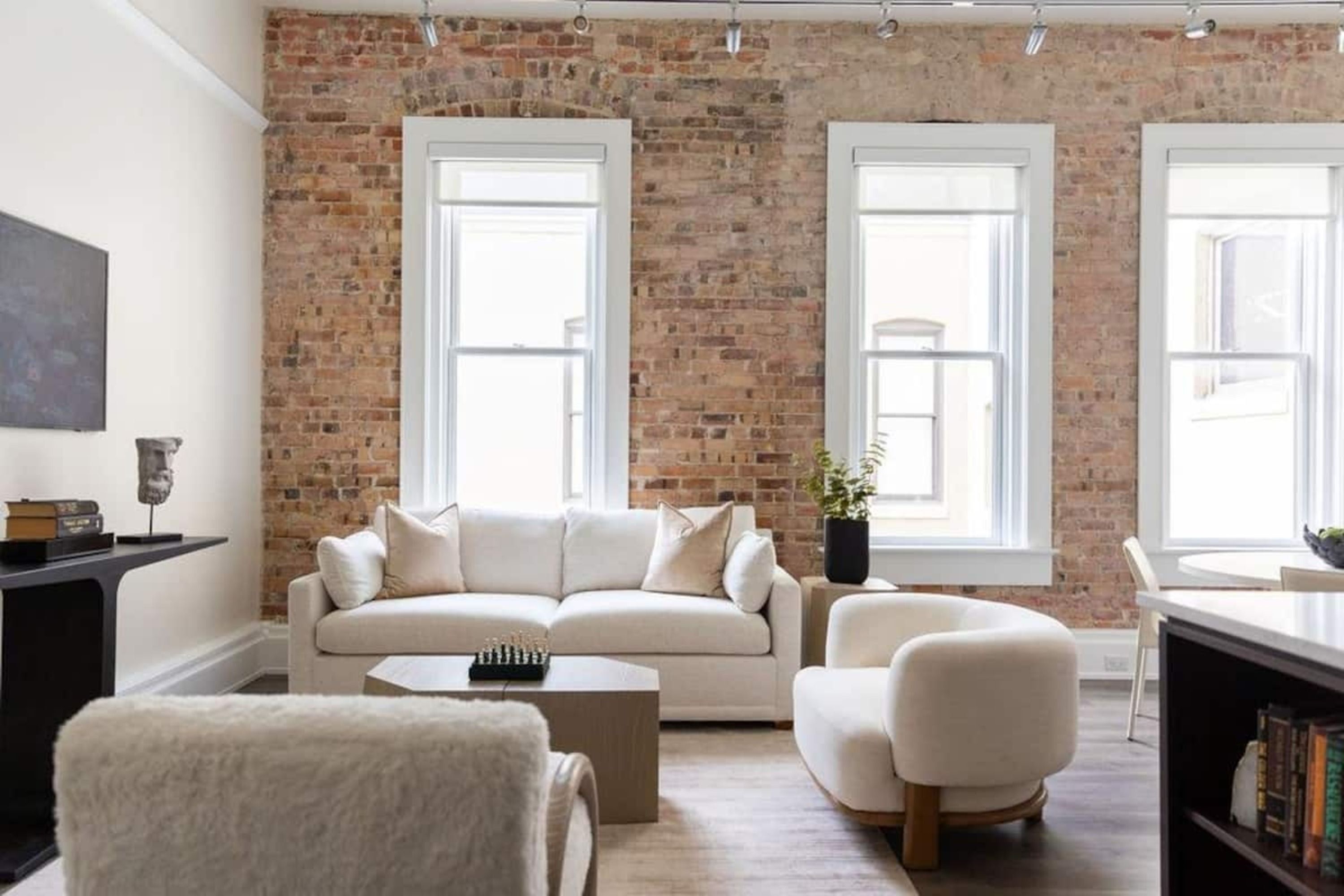 A living room with a brick wall, white sofa, armchair, and a coffee table.