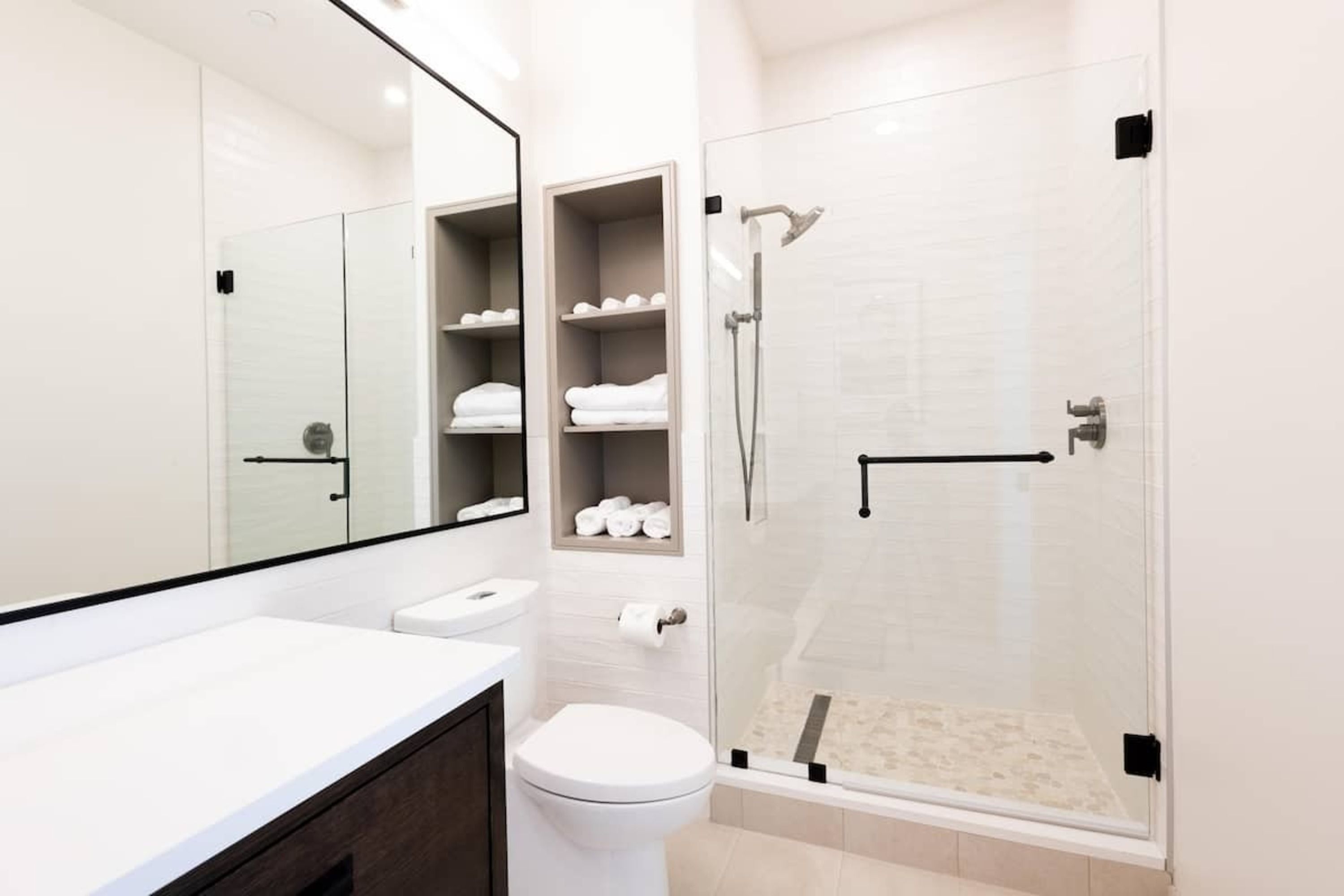 A modern bathroom with a glass-enclosed shower, white fixtures, and a large mirror.