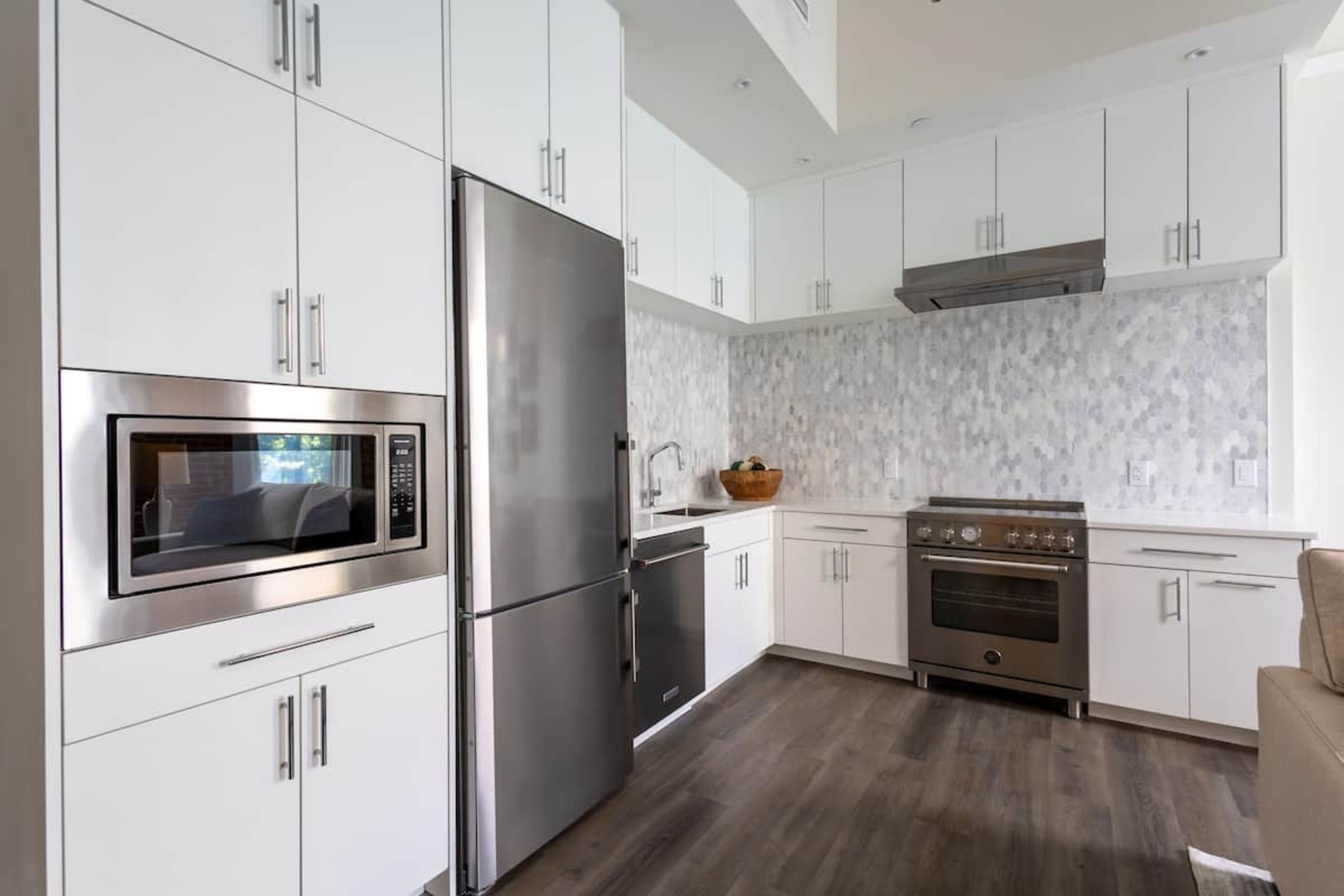 A modern kitchen with stainless steel appliances, white cabinetry, and a wood floor.