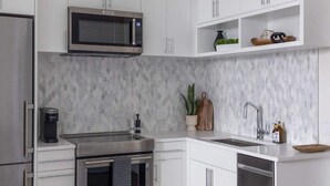 Een moderne keuken met witte kasten, een ingebouwde magnetron, roestvrijstalen apparatuur en een spatwand.
