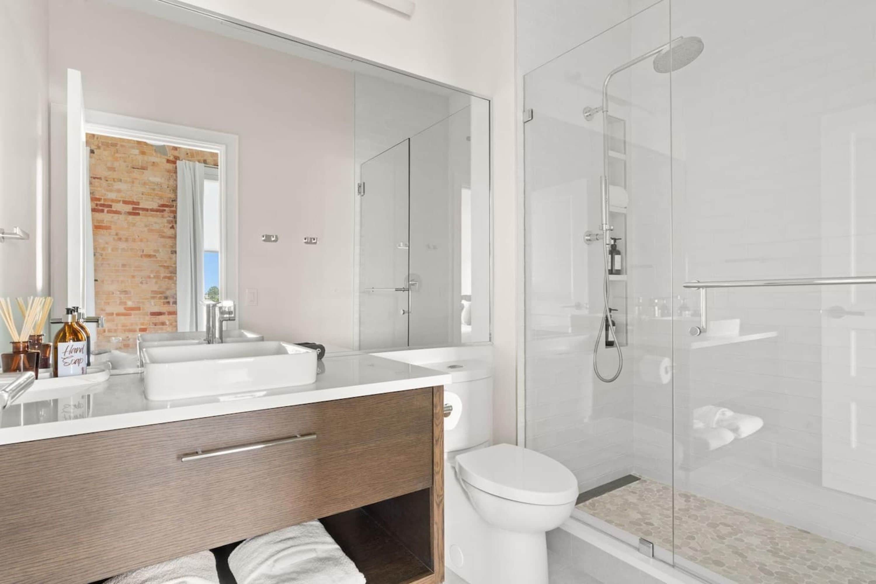 Een moderne badkamer met een douchecabine van glas, een grote spiegel en een houten wastafelmeubel.