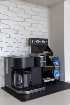 Una cafetera con un cartel de cafetería, una cafetera Keurig y un saco de granos de café.