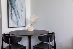 Een ronde tafel met twee stoelen, een vaas met pluimgras en een groot abstract schilderij aan de muur.