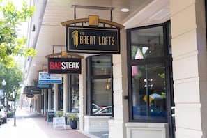 Una calle con diversas tiendas, incluyendo 'The Brent Lofts' y 'Bar Steak'.