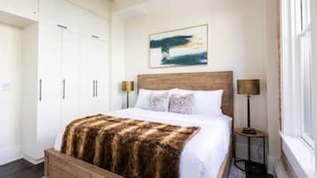 Un dormitorio con cama de madera, paredes blancas, un cuadro grande y una mesita de noche con lámpara.