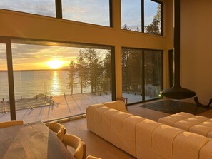 A modern living room with large windows overlooking a body of water at sunset. - Luxury Georgian Bay Cottage – 3 Bed, 5 Bath, Tiny Township (Tiny)