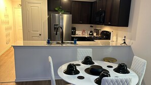 A modern kitchen with dark cabinets, a stainless steel refrigerator, and a white dining table with black centerpieces. - Cozy Hideaway with Pool – Relax & Unwind Just Off the Highway (Maxwell)