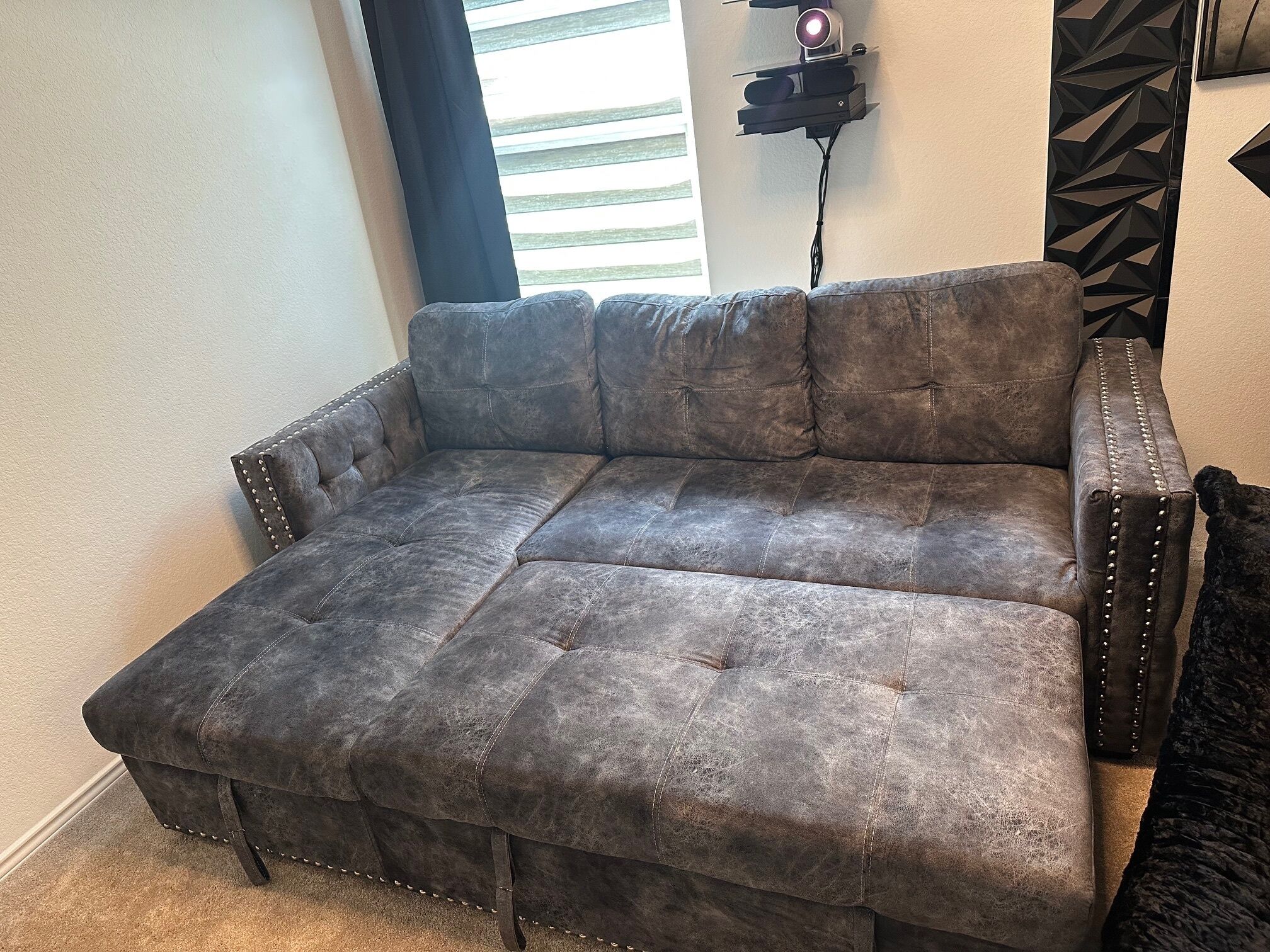 A grey sectional sofa with a tufted design, positioned against a wall with a geometric patterned accent.