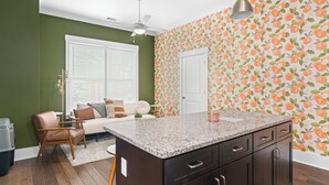 A kitchen with a granite countertop, dark cabinets, and a window with blinds. - The Peach House- Near Downtown (Savannah)