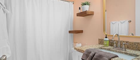A bathroom with a white toilet, a shower curtain, a sink with a granite countertop, a mirror, and a towel rack.