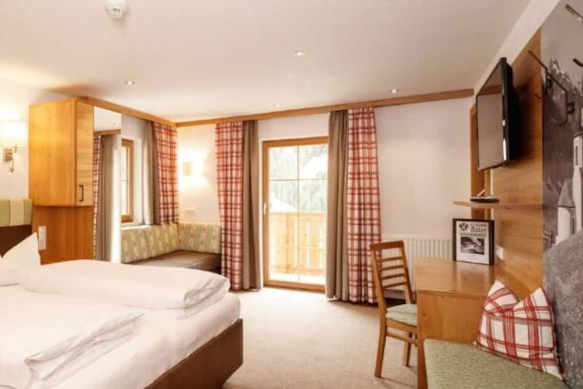 A hotel room with a bed, a desk, a chair, a TV, and a window with curtains.
