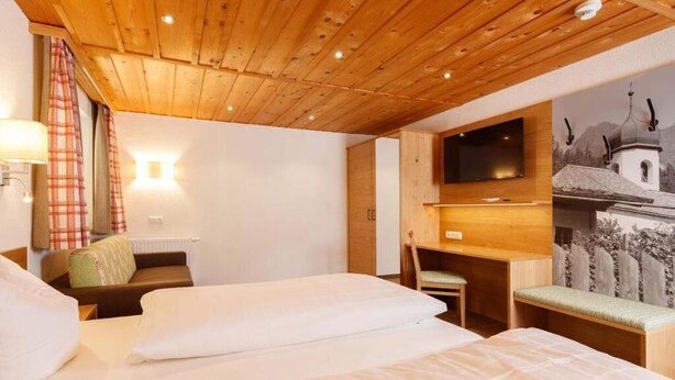 A hotel room with wooden ceiling, two beds, a desk, a chair, a TV, and a wall-mounted artwork. - Landgasthof Adler (Hinterhornbach)
