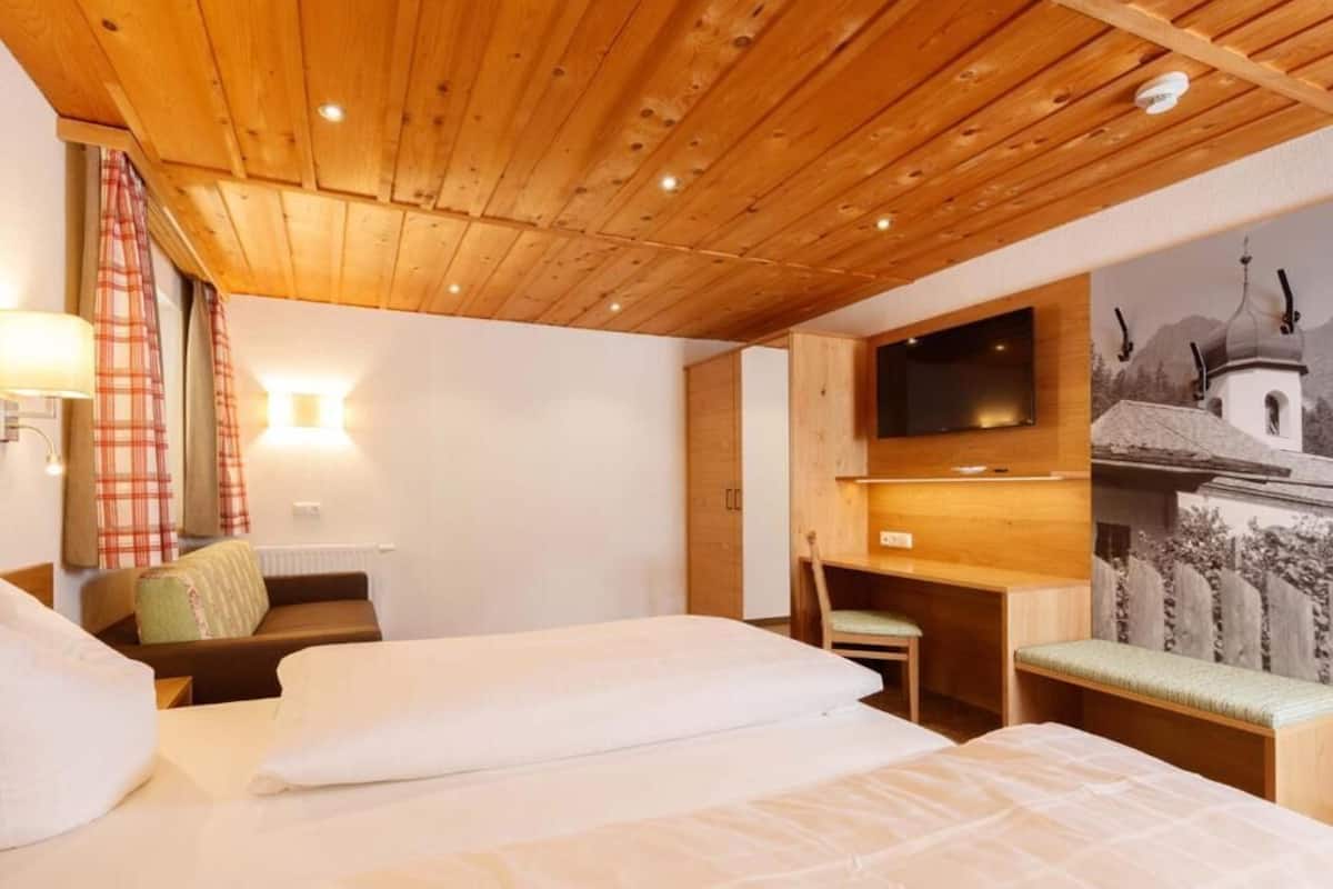 A hotel room with wooden ceiling, two beds, a desk, a chair, a TV, and a wall-mounted artwork.