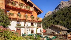 A wooden building with balconies, outdoor seating, and a mountain backdrop. - Landgasthof Adler (Hinterhornbach)