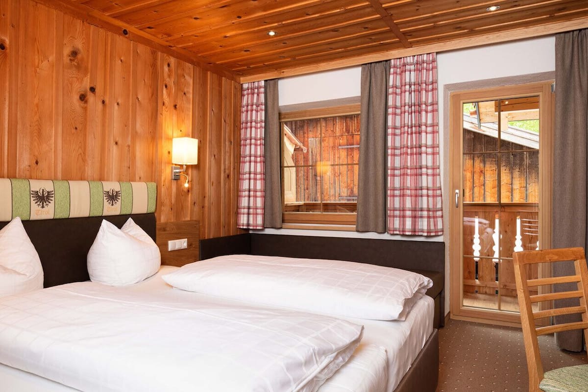 A wooden cabin room with two beds, a chair, and a window with curtains.