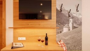 A wooden interior with a mounted TV, a small table with a bottle and glasses, and a framed picture on the wall. - Landgasthof Adler (Hinterhornbach)