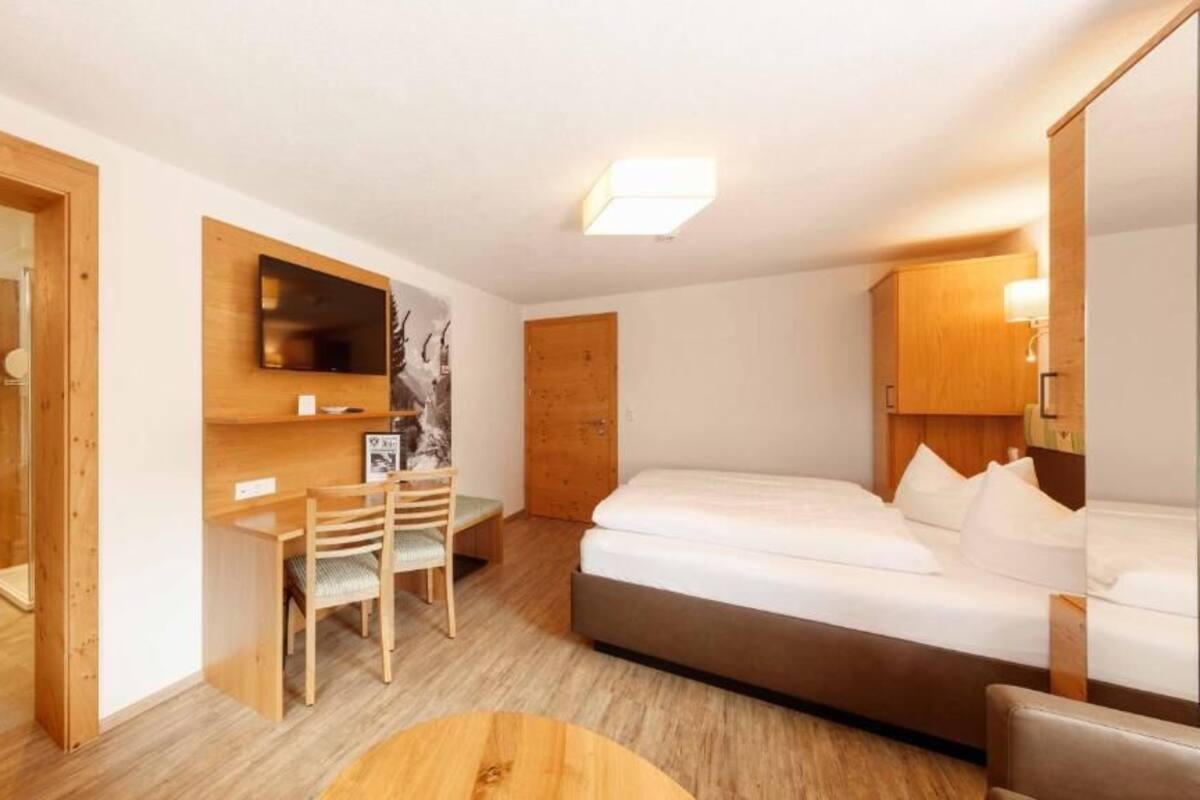 A hotel room with a bed, a desk, a chair, a TV, and a wooden cabinet.