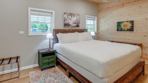 A bedroom with a wooden bed, a nightstand, a green dresser, and two windows with blinds. - Southern Comfort Near Historic Dtwn Rockmart (Rockmart)