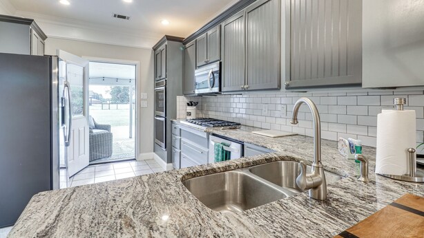 A modern kitchen with granite countertops, stainless steel appliances, and grey cabinetry. - Southern Comfort Near Historic Dtwn Rockmart (Rockmart)