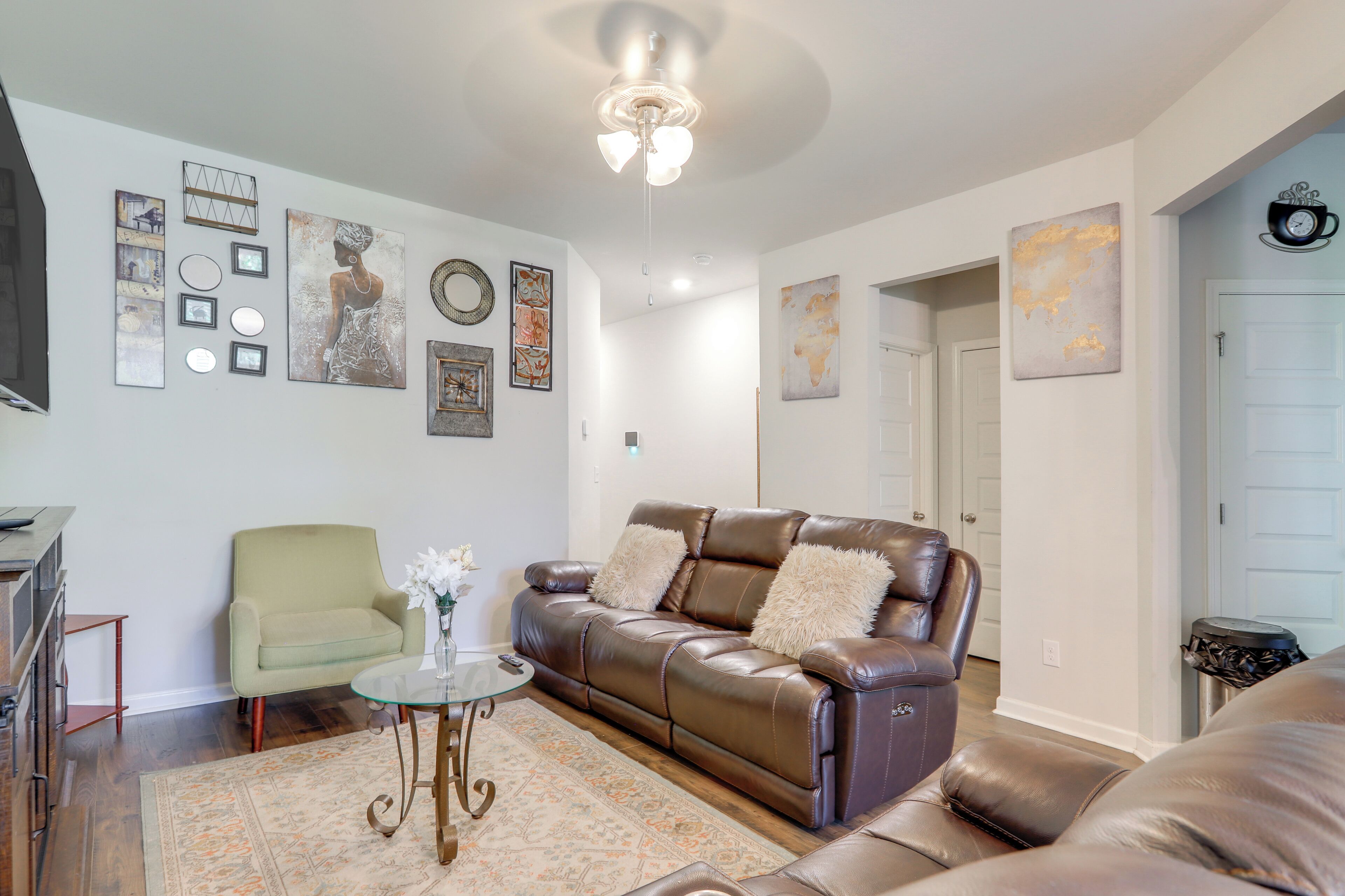 Ein Wohnzimmer mit braunem Ledersofa, einem grünen Sessel und einem Glastisch. An den Wänden befinden sich Dekorationen, darunter gerahmte Bilder und ein Globus.