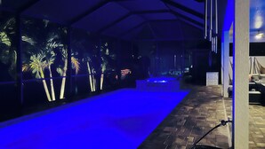 Un espace piscine intérieure doté d’un sol illuminé de lumière bleue, d’un tuyau d’arrosage sur la droite et d’un mur orné d’une fresque aux motifs tropicaux.