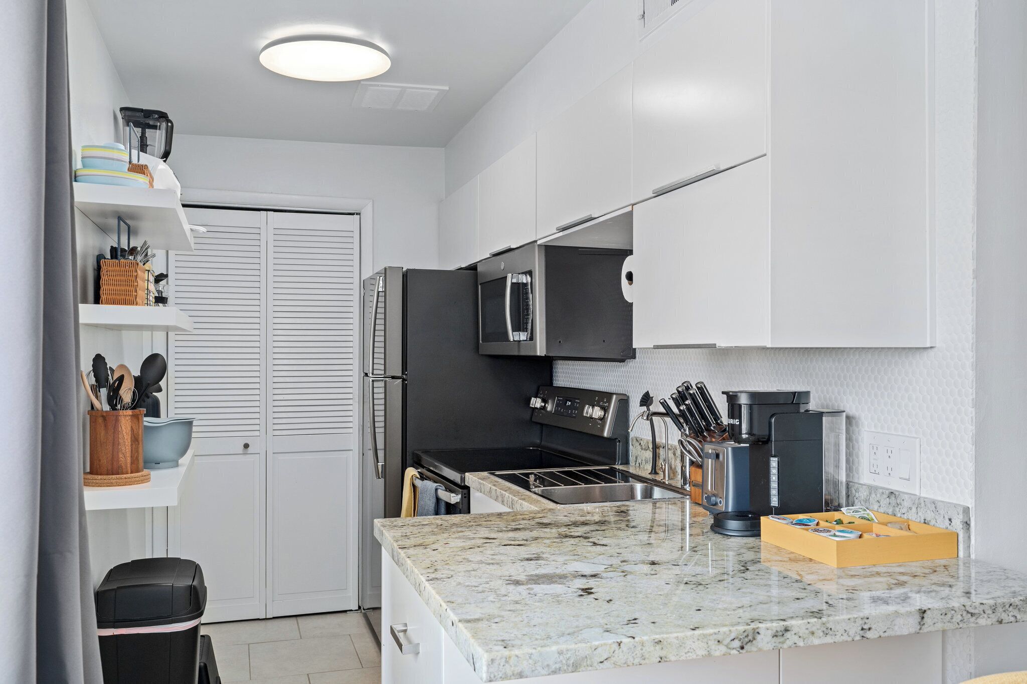 A modern kitchen with white cabinets, a black refrigerator, a built-in oven, and a granite countertop.