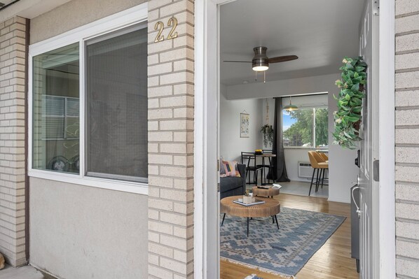 A modern interior with a large window, a door with the number 22, a ceiling fan, and a dining area with a table and chairs.