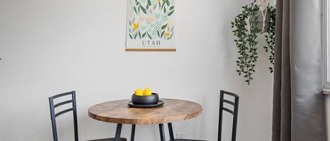 A dining area with a round wooden table, two black chairs, and a hanging macrame plant.