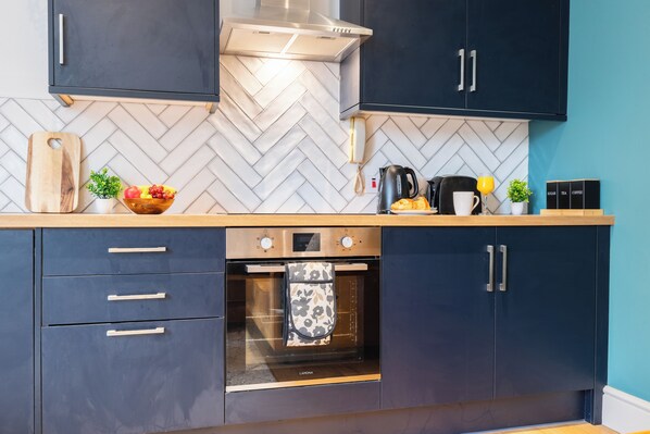 A modern kitchen with dark cabinets, a herringbone-patterned backsplash, and a built-in oven. - The Ground Floor Getaway (Cardiff)