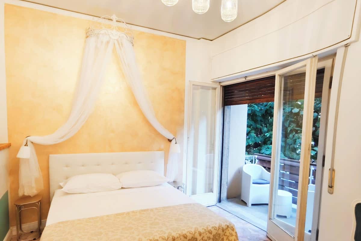 A bedroom with a large bed, a canopy, a chandelier, and a view through a sliding glass door.