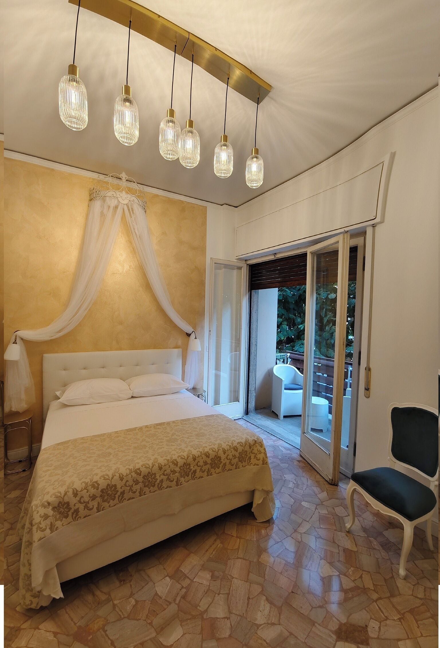 Ein Schlafzimmer mit einem großen Bett, einem Baldachin, einer Schiebetür zu einem Balkon und einem Sessel.