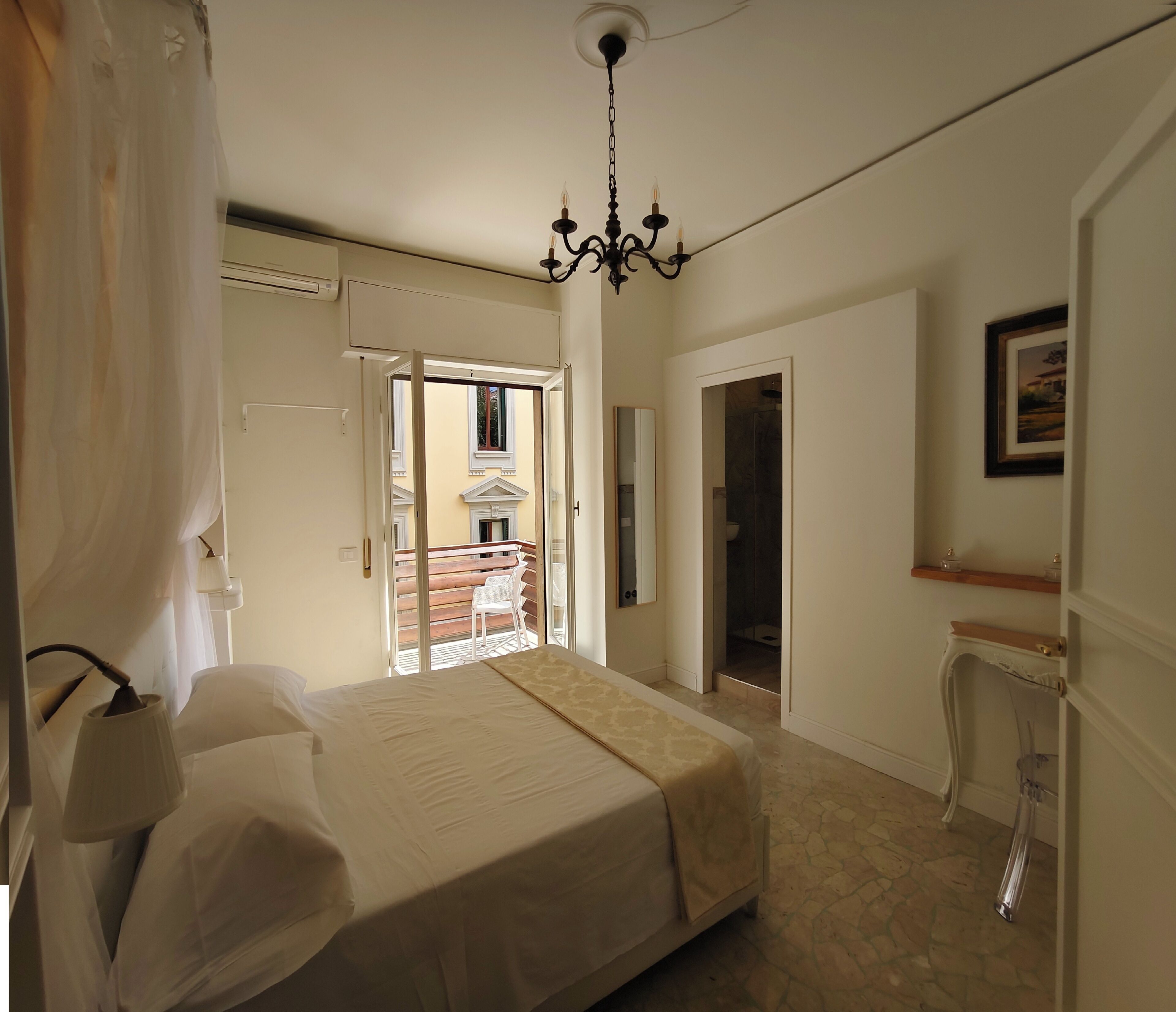 A bedroom with a bed, a chandelier, a bathroom, and a balcony.