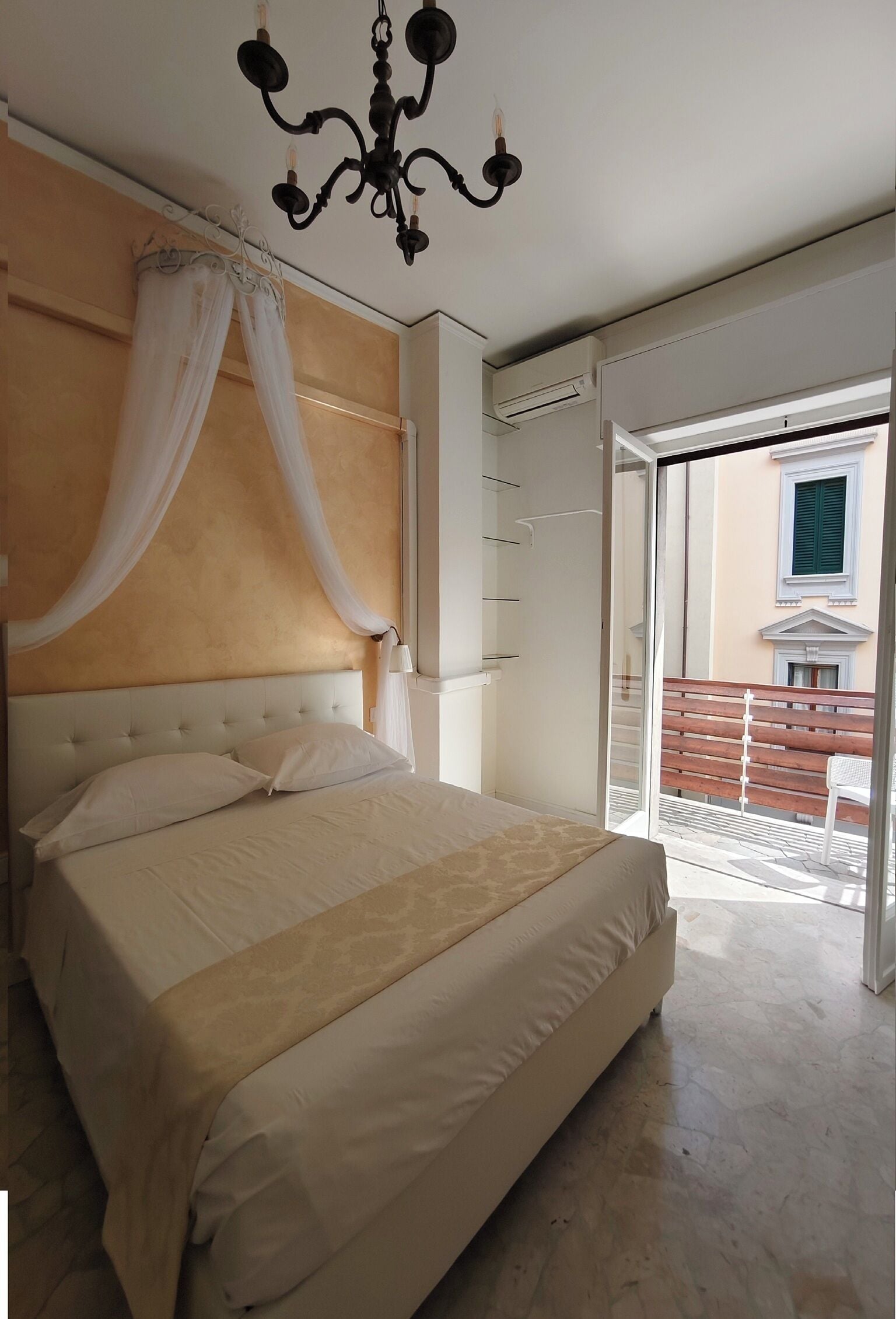 A bedroom with a large bed, a chandelier, and a view of the outside balcony.