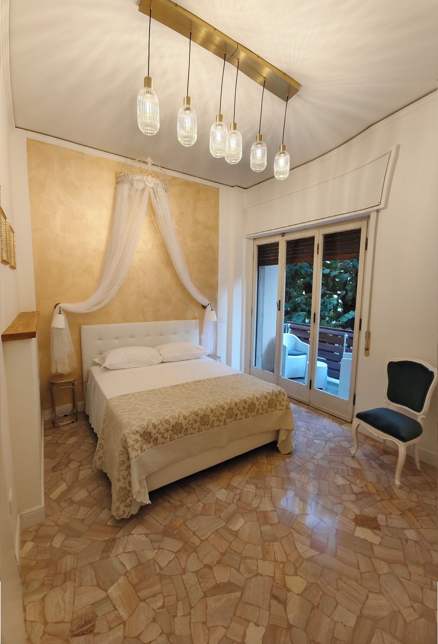 Quarto com cama, uma cadeira, mesa de cabeceira, abajur e porta de vidro deslizante que dá para uma área externa.