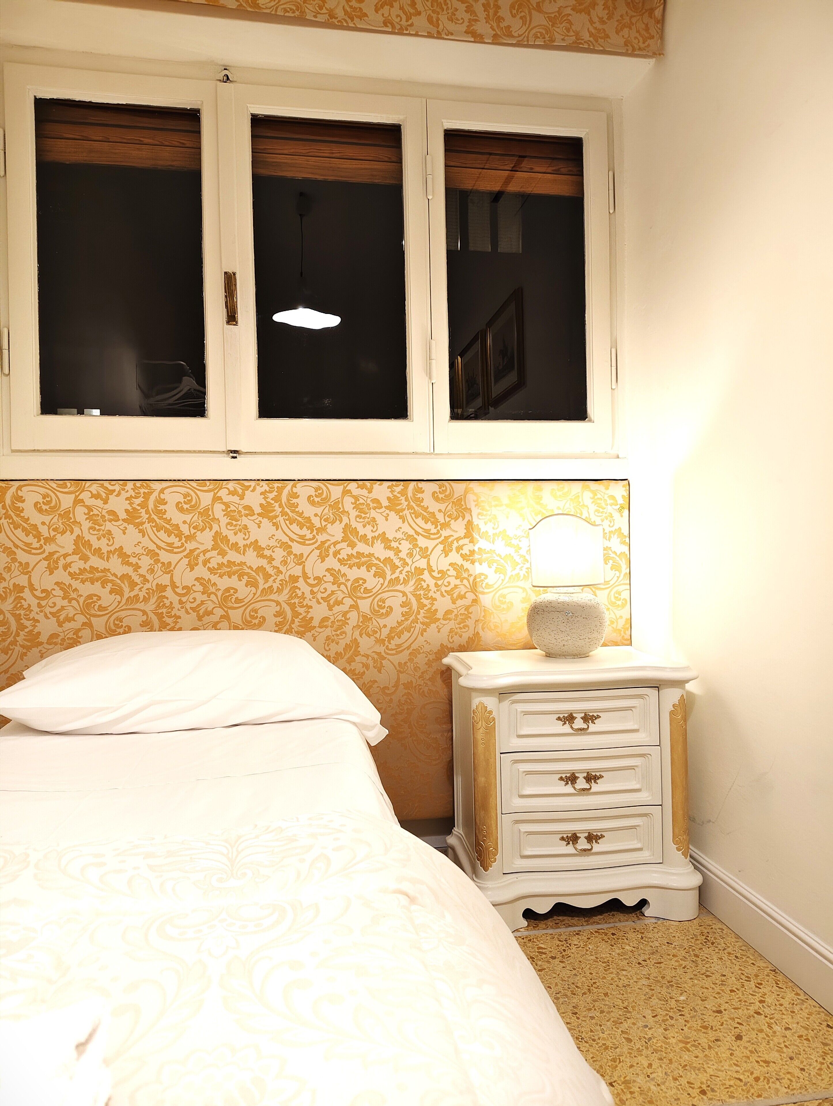 A bedroom with a bed, a nightstand, and a window with a view of the outside.