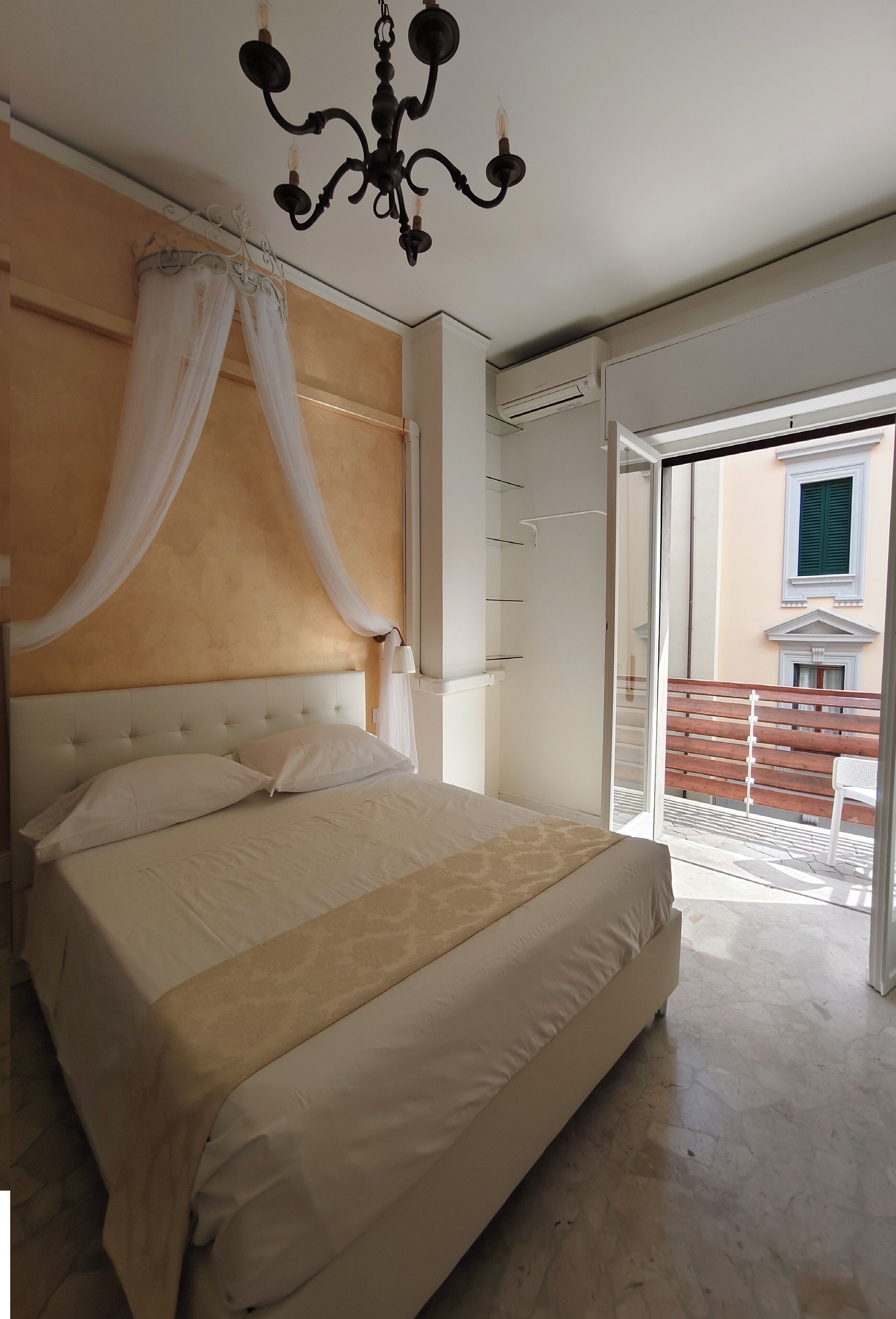 Quarto com uma cama grande, um candelabro e vista para a varanda.