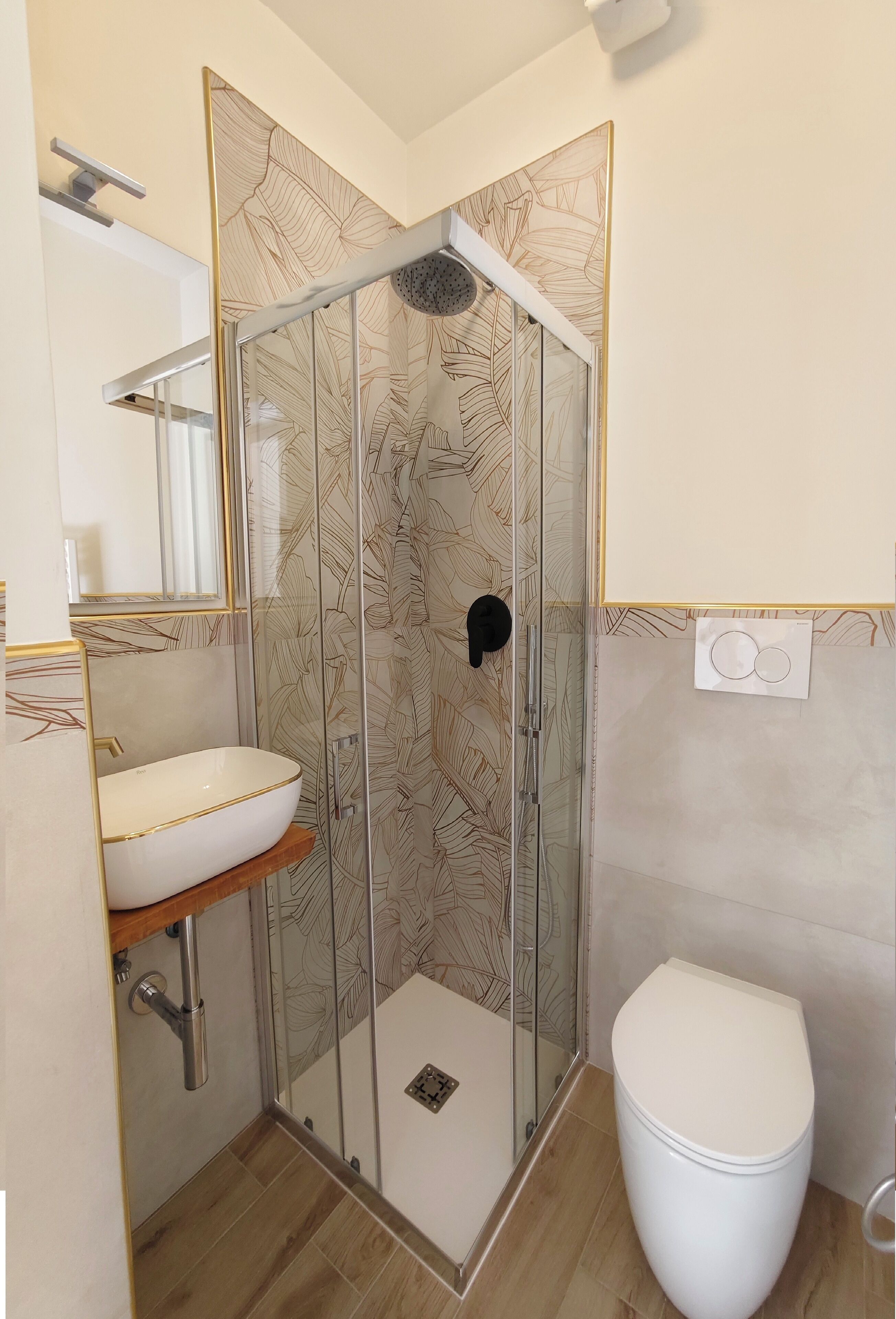 Un baño con cabina de ducha de vidrio, lavamanos blanco con detalles dorados y inodoro blanco.