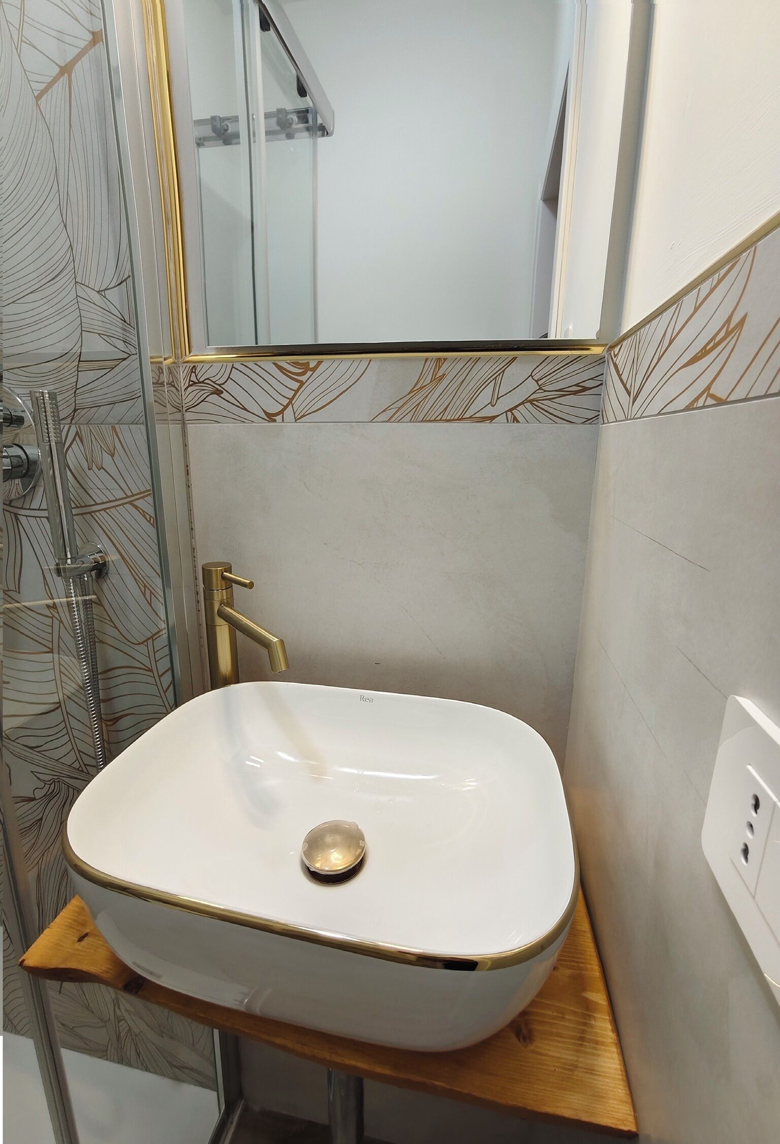 Une salle de bain avec un lavabo blanc, un robinet doré et une douche dotée d’une porte en verre.