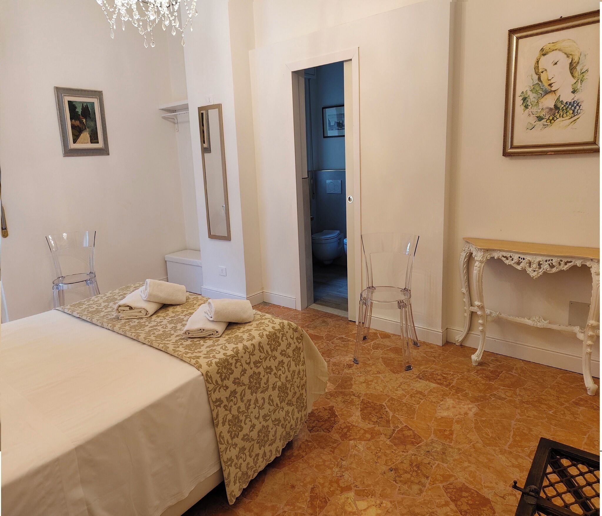 Un dormitorio con cama, una silla, tocador y una puerta que da a un baño.