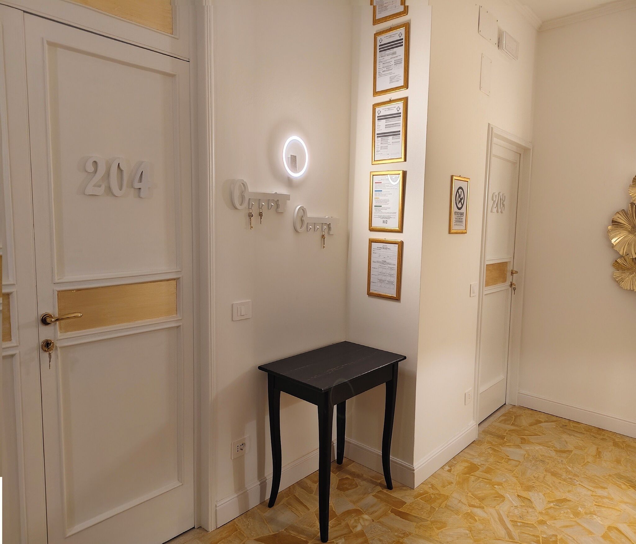 A hallway with doors numbered 204 and 218, a small table, and wall-mounted keys and certificates.