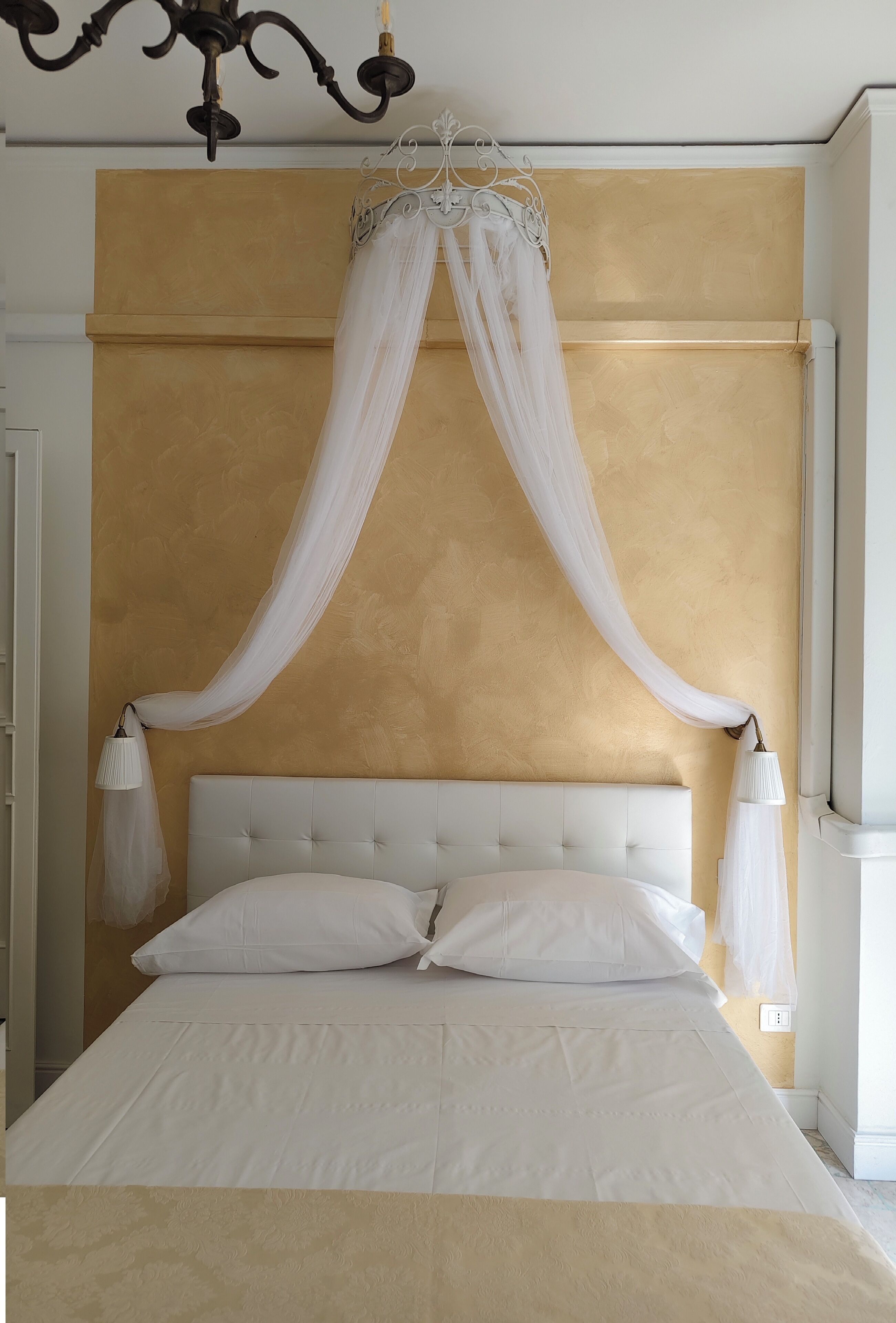 A bedroom with a white canopy bed, a tufted headboard, and bedside lamps.