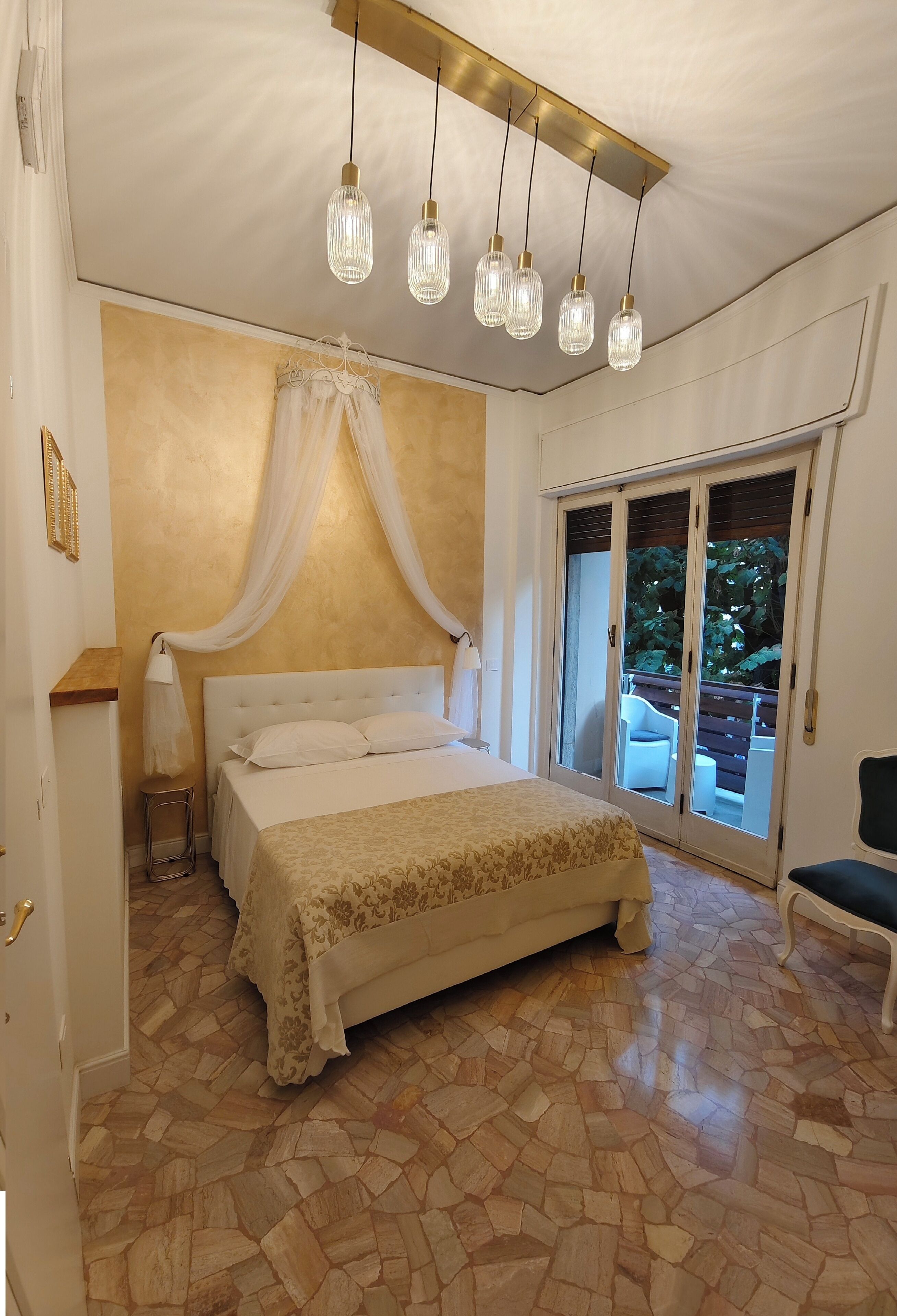 Une chambre à coucher comprenant un lit, une table de chevet, une chaise, un luminaire au plafond et une porte-fenêtre coulissante donnant sur un espace extérieur.
