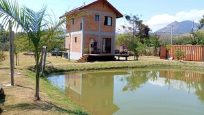 Une maison à deux étages, construite en briques, avec une petite terrasse et un étang devant.
