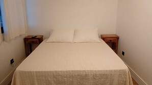 Un lit recouvert d’une couvre-lit blanche, avec deux oreillers et deux tables de chevet en bois, une de chaque côté.