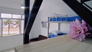 Een kamer met een stapelbed, een raam met uitzicht op palmbomen en een houten tafel met een roze bloem.