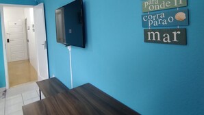 Een kamer met een blauwe wand, een flatscreen televisie aan de wand bevestigd, en een houten bank.