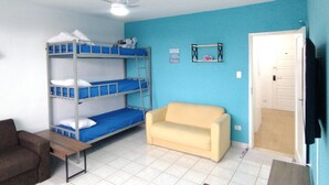 Een kamer met stapelbedden, een slaapbank, een klein tafeltje en een plafondventilator.